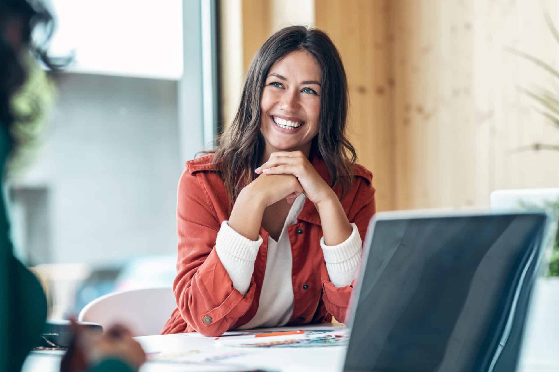 Shot of smiling young business woman listening her partner on coworking space.